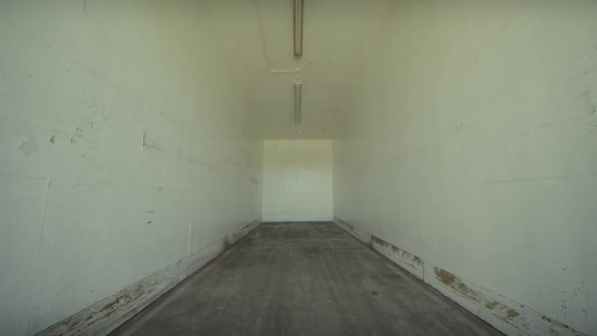 A slow camera pull-out reveals an empty and stark white industrial corridor with fluorescent lighting