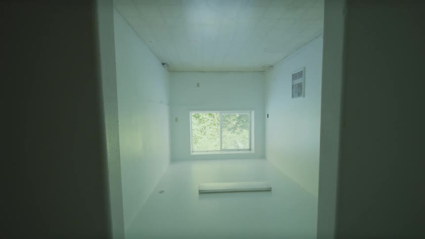 A disorienting slow pull-back shot reveals a sterile, white room that is completely upside down, viewed from below
