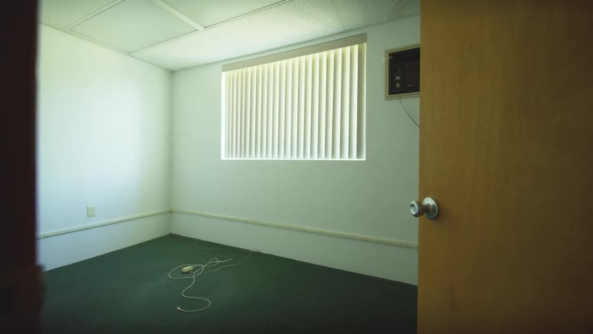 A slow and eerie pull-back shot from an empty, sunlit office room with a stray cord on the floor