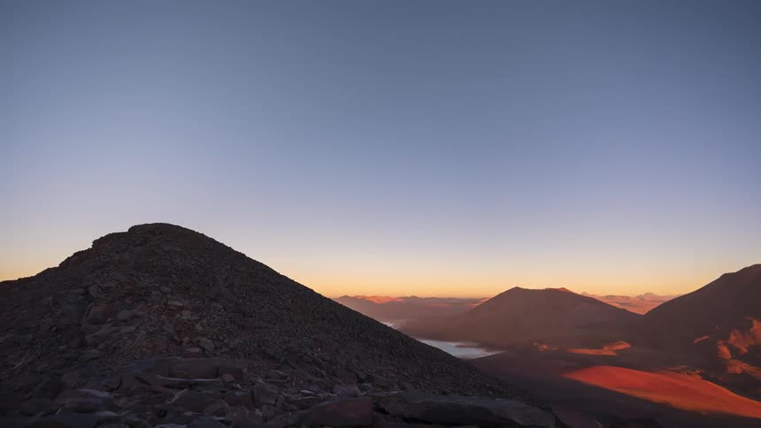 A stunning day-to-night time-lapse reveals a brilliant starry sky and the Milky Way galaxy over volcanic mountains in a vast desert landscape