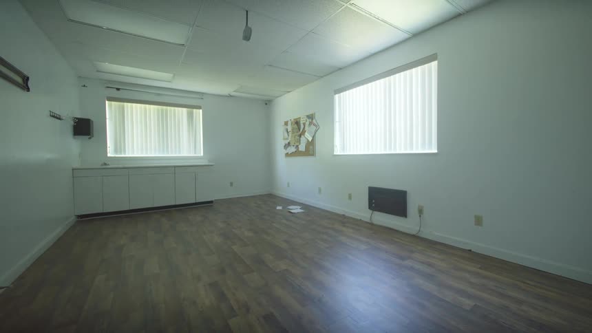 A slow pull back reveals the interior of a vacant and desolate office space with laminate flooring and white walls