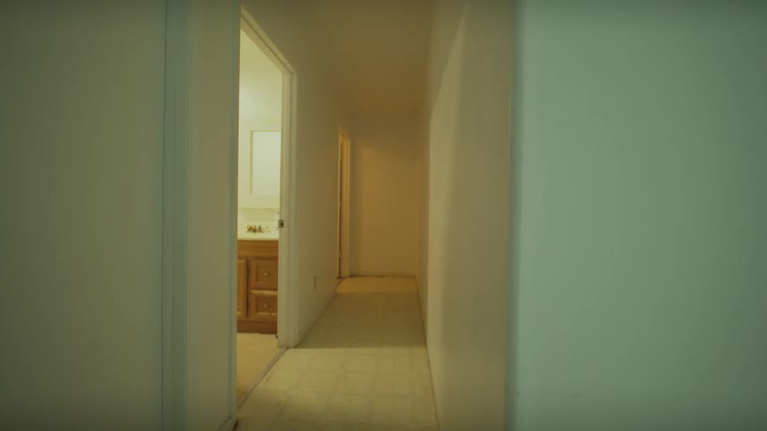A steady shot captures a quiet and empty hallway with white walls and a visible bathroom at the far end