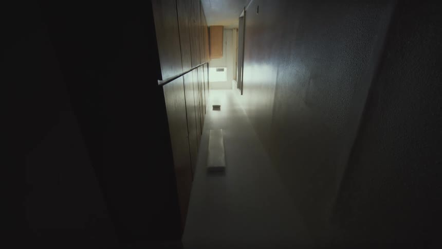 A suspenseful, slow pull-back shot from a high angle reveals a dark and eerie interior hallway
