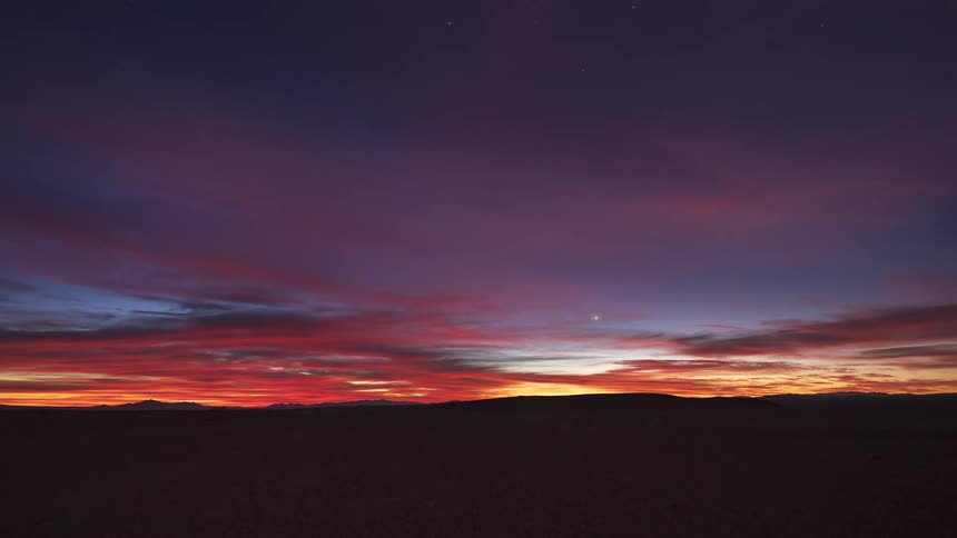 A stunning timelapse captures a fiery sunset over a vast desert landscape as the day transitions to a star-filled night