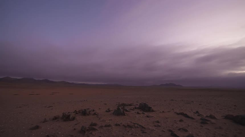 A stunning day-to-night time-lapse of the sun setting over a vast, arid desert landscape as clouds roll in