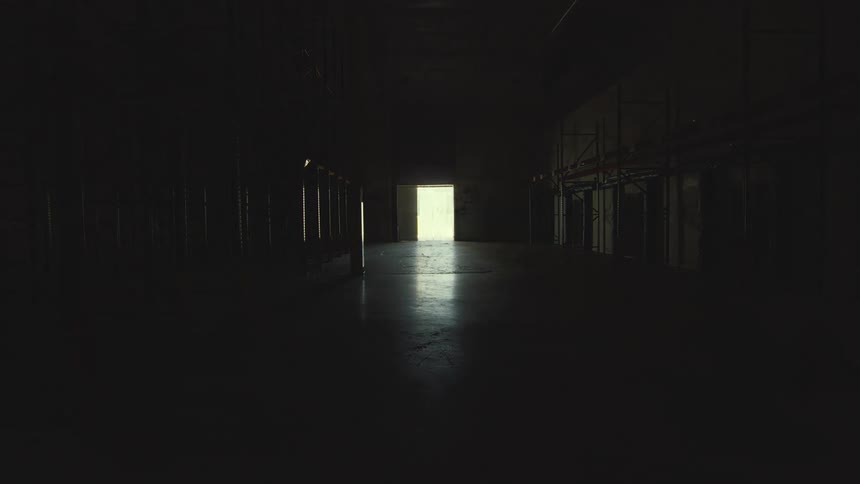 Light gradually illuminates the vast, empty interior of an abandoned industrial warehouse with metal shelving