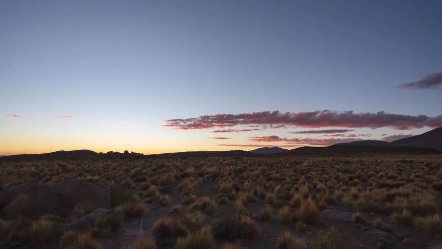 A stunning timelapse captures the transition from day to night as the sun sets over a vast, grassy plain, revealing a beautiful starry sky
