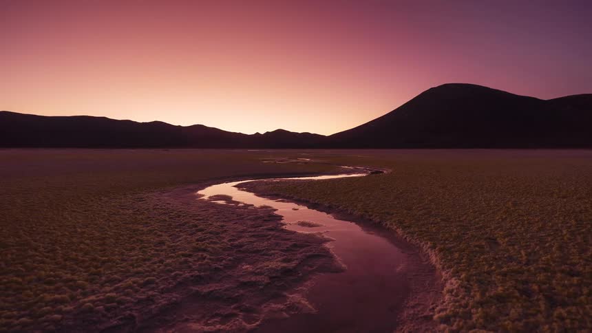 A stunning day-to-night timelapse captures the sun setting over a surreal yellow salt flat with a winding river, revealing a brilliant starry sky