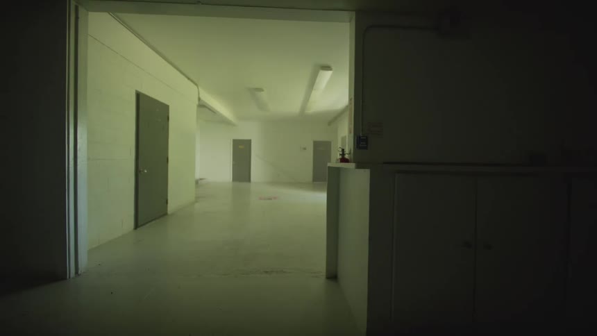A slow pan reveals the empty, dimly lit interior of an abandoned institutional building