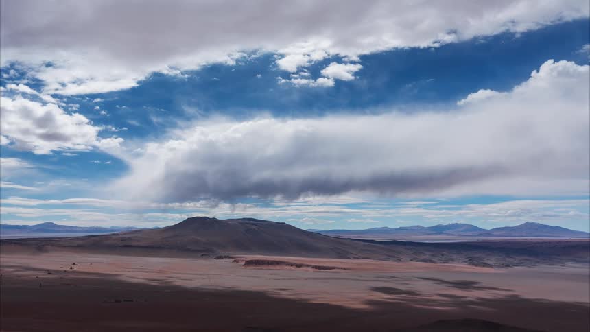 An epic aerial time-lapse shows majestic clouds and their shadows sweeping across a vast, barren desert landscape with distant mountains
