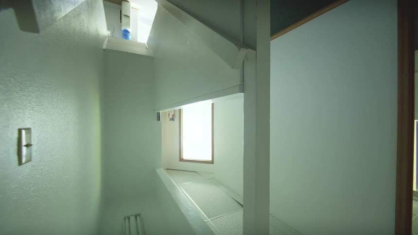 Slow pan shot of a minimalist, white-walled empty hallway inside a home, filmed in vertical orientation
