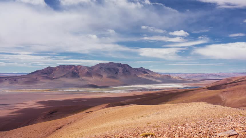 Time-lapse of clouds casting shadows over a vast, arid mountain valley landscape in the Andes