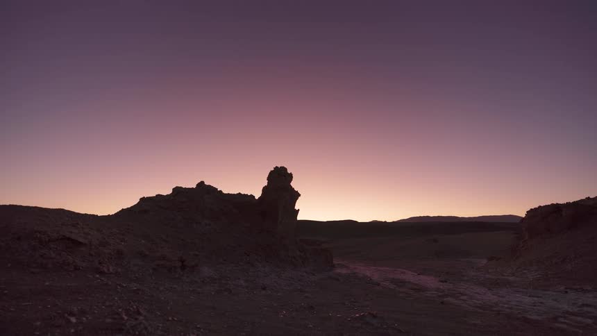 A breathtaking timelapse shows the sun setting behind a rocky formation in the desert, transitioning from a clear day to a beautiful purple twilight and a starry night sky