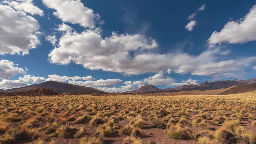 Cinemagraph time-lapse of white clouds drifting across a deep blue sky over a vast, arid mountain landscape