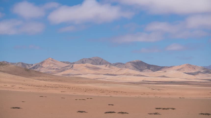 A stunning timelapse of clouds moving over a vast, arid desert and mountain landscape under a bright blue sky