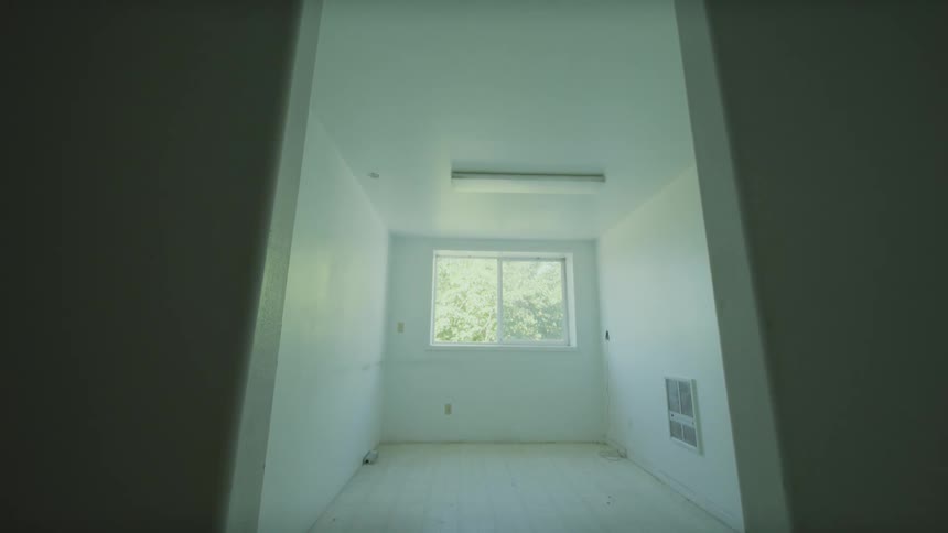 A slow camera tilt up from the floor of a dark hallway reveals an empty, white-walled room with a window