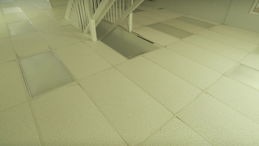A slow, eerie pan across a damaged drop ceiling with missing tiles in an abandoned, unfinished room