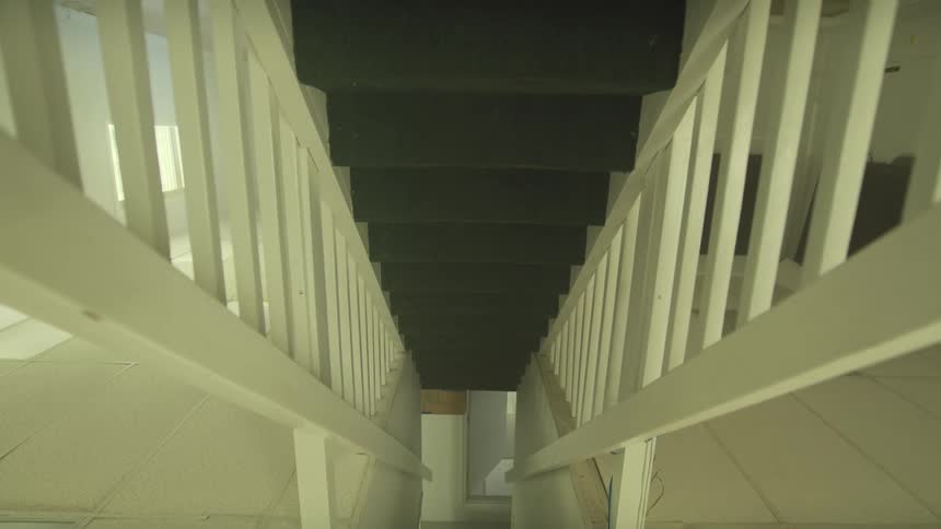A slow and eerie top-down zoom-out reveals a dark, carpeted staircase leading downwards