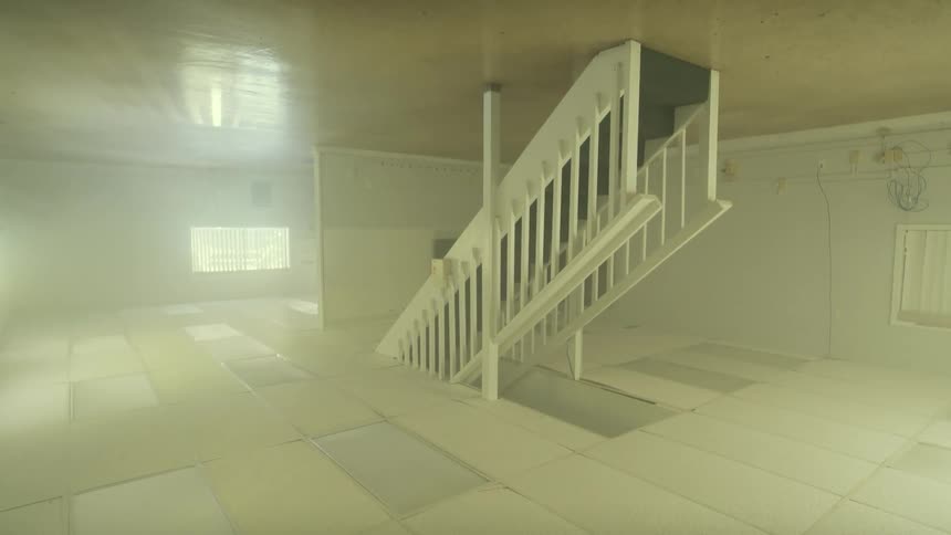 A disorienting slow reveal of a foggy and empty upside-down room with a staircase on the ceiling