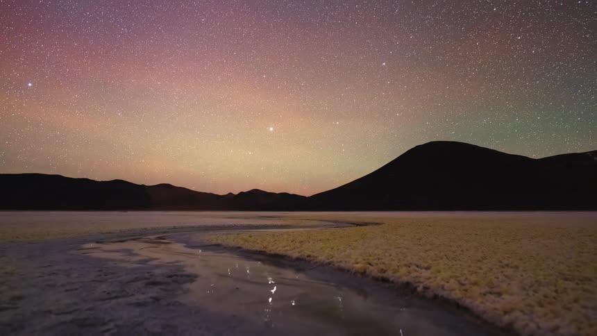 An epic night-to-day timelapse captures the moon setting, the Milky Way glowing, and the sun rising over a surreal high-altitude salt flat