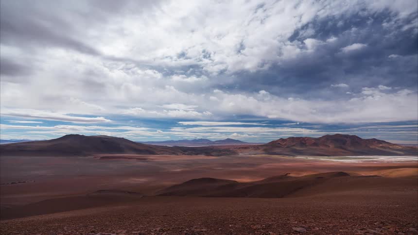 A dramatic timelapse of clouds casting moving shadows across a vast and remote desert landscape