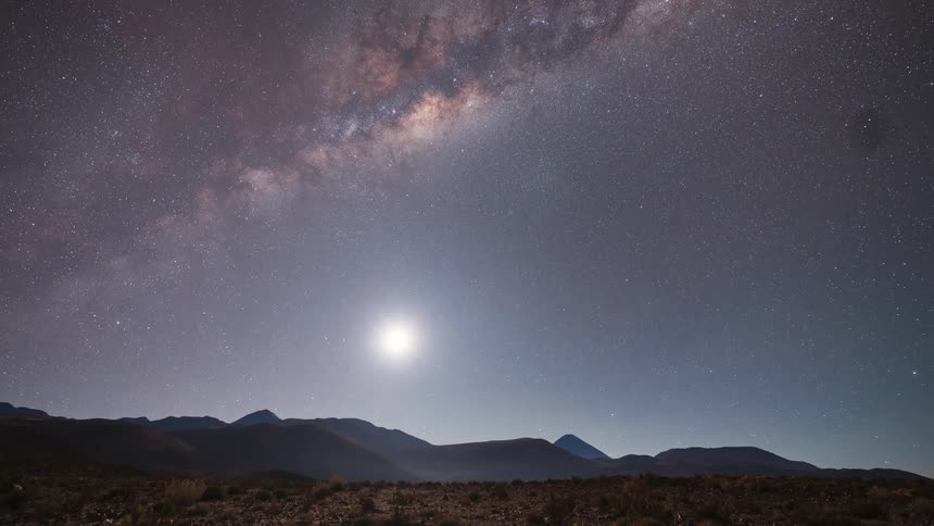 A spectacular time-lapse captures the Milky Way and a moonrise transitioning to a brilliant sunrise over a vast desert mountain landscape
