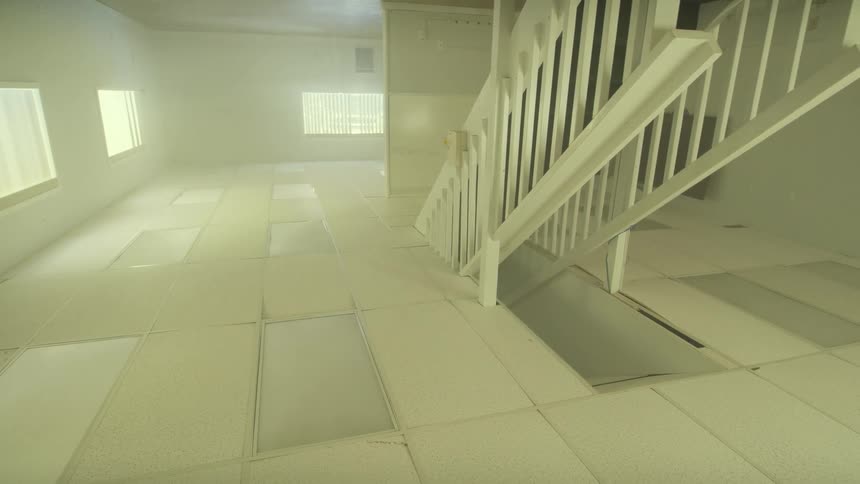 Disorienting pan across a foggy, stark white, upside-down room with a staircase descending through the ceiling