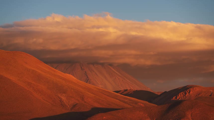 Clouds roll over a desert mountain peak in a spectacular sunset timelapse, illuminating the landscape in golden and crimson hues