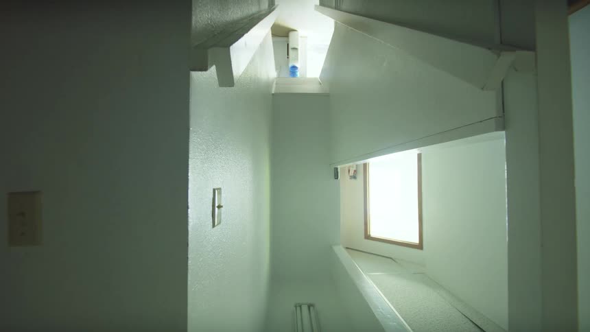 An upward dolly shot ascends through a narrow, modern, white stairwell with dark wooden stairs
