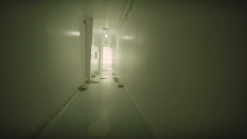 A point of view shot down a long, narrow, institutional hallway as the lights flicker on and off erratically