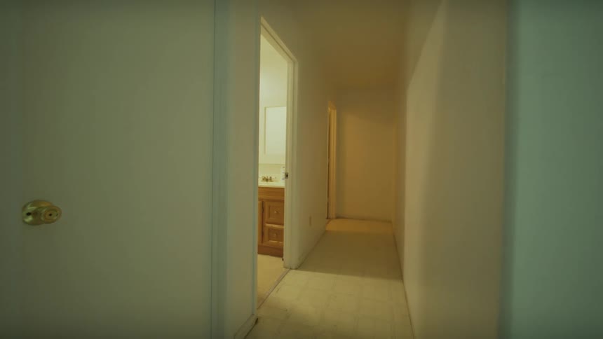 A slow pull back shot from a white wall reveals an empty hallway leading to a bathroom