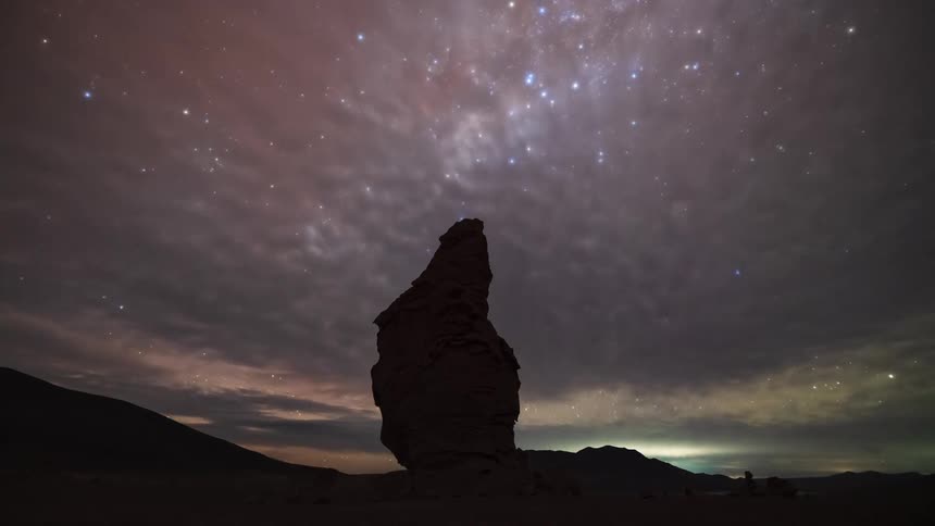 A stunning day-to-night-to-day timelapse shows the sun setting, the Milky Way rising, and a fiery sunrise over a lone rock formation in a vast desert landscape
