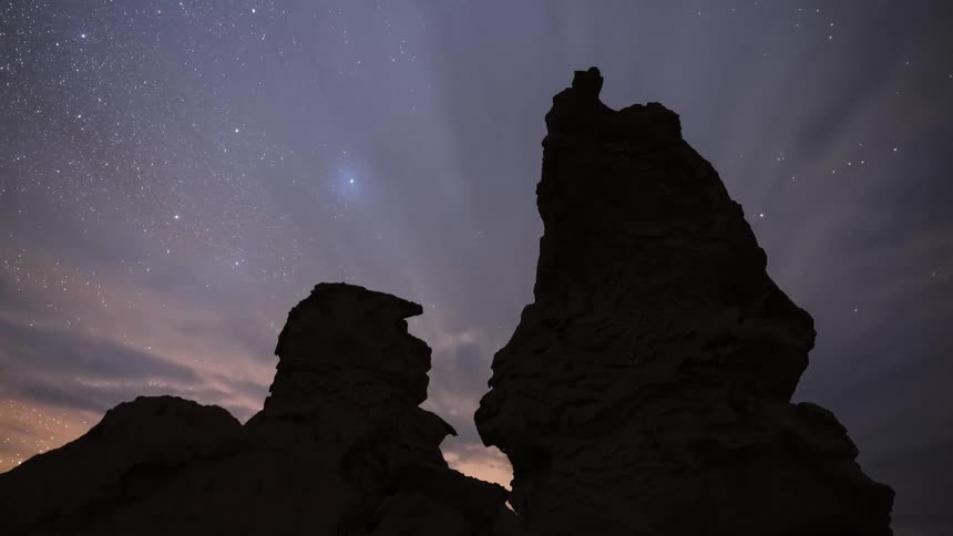 A stunning night-to-day timelapse shows the Milky Way and stars rotating above silhouetted desert rock formations until sunrise illuminates the landscape