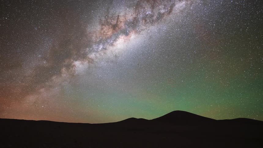 A stunning day-to-night-to-day timelapse over a desolate desert landscape reveals the vibrant Milky Way and a colorful, starry sky