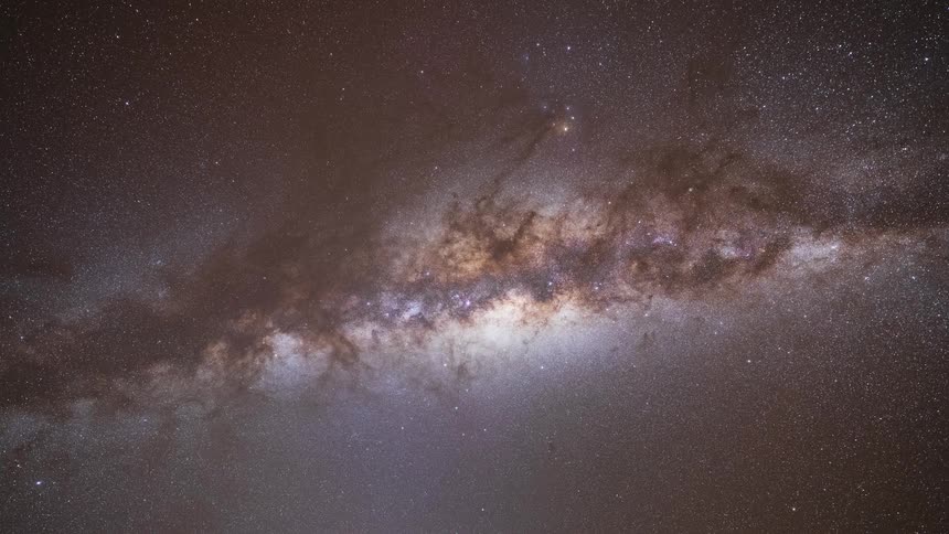 A stunning time-lapse shows the Milky Way galaxy moving across the night sky behind a rocky desert cliff before transitioning into a clear blue day