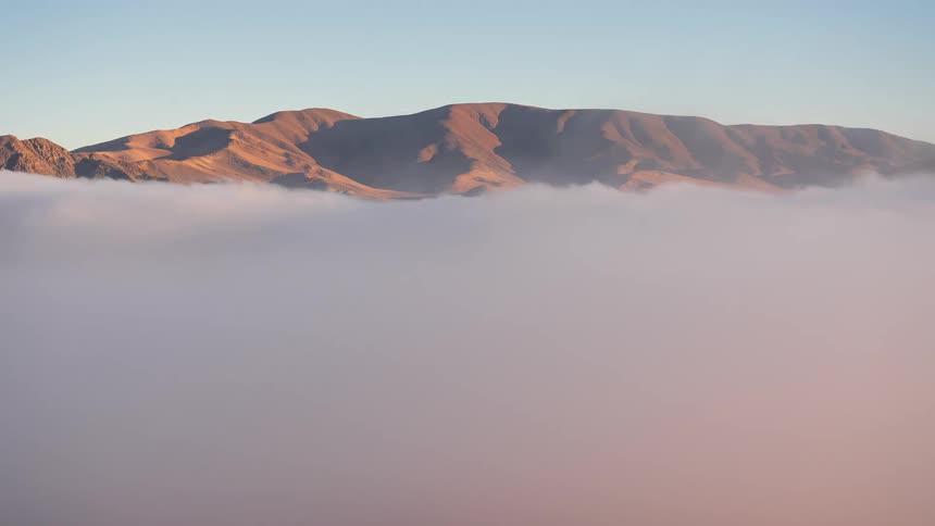 A breathtaking timelapse shows a sea of fog rolling through a desert valley at sunrise, illuminating distant mountain peaks