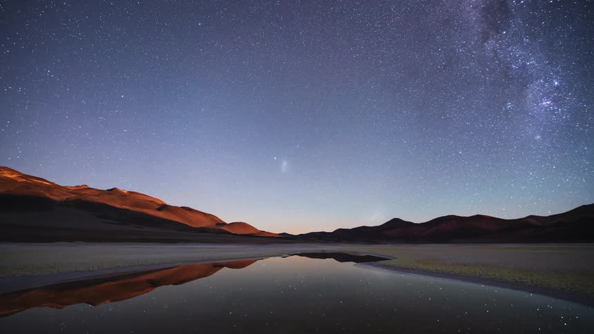 Stunning night-to-day time-lapse shows the Milky Way and stars reflecting in a desert lake before a beautiful sunrise illuminates the mountain landscape
