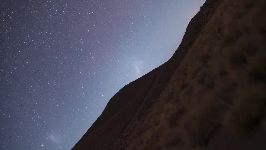 Holy grail timelapse zooms from the Large Magellanic Cloud in a starry night sky to a vibrant sunrise over a mountainous landscape