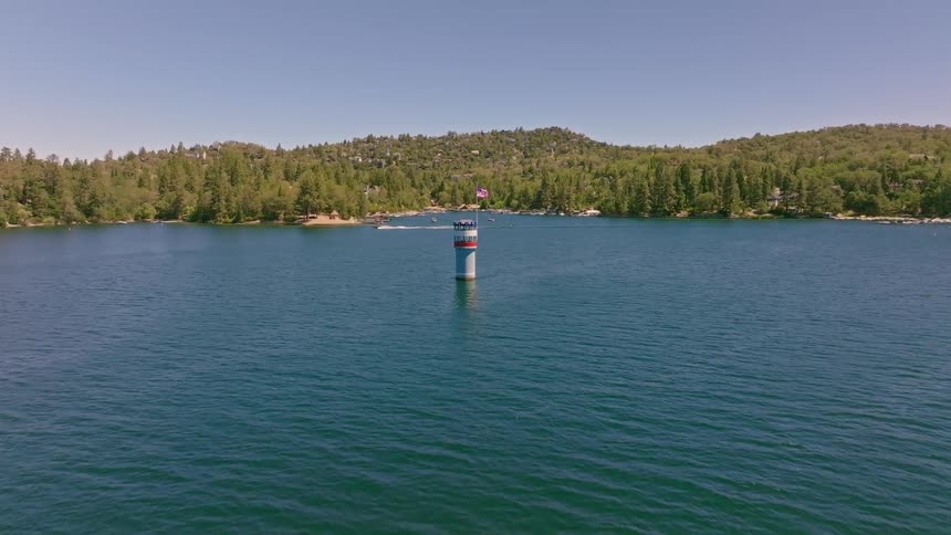Aerial view slowly approaching a patriotic lighthouse flying an American flag in the middle of a scenic mountain lake
