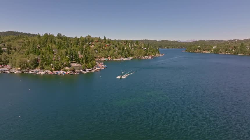 An aerial view captures a person water skiing behind a motorboat on a beautiful mountain lake on a sunny day