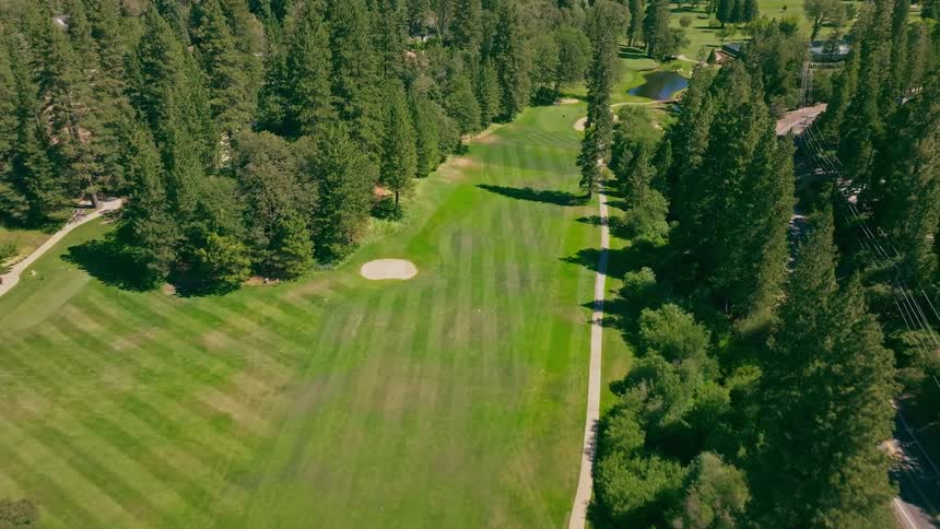 A scenic aerial journey over a beautiful golf course surrounded by a lush forest on a bright, sunny day