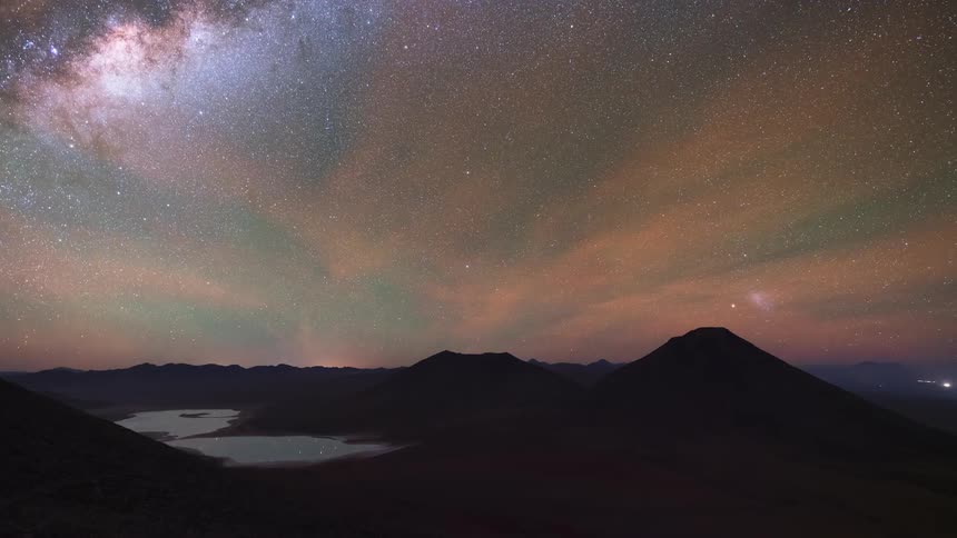 A stunning day-to-night-to-day time-lapse over volcanoes and a desert lake, revealing the Milky Way galaxy and a vibrant starry sky