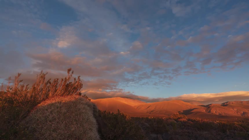 A stunning timelapse of a vibrant sunset over a desert landscape, with clouds painting the sky in shades of orange and pink above the mountains