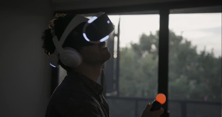 A man looks around as he uses a vr headset and controllers