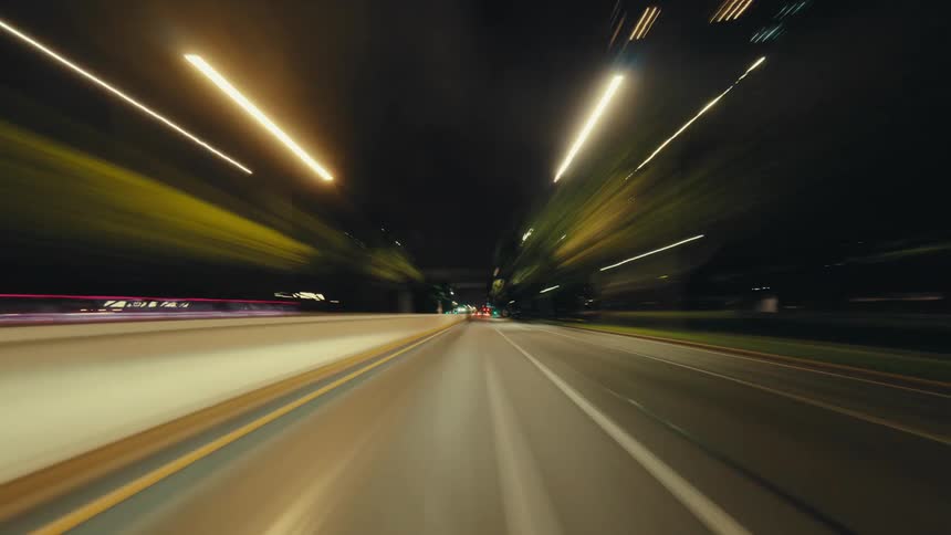 First-person perspective hyper-lapse of driving down an urban highway at night, with street lights blurring into streaks of light