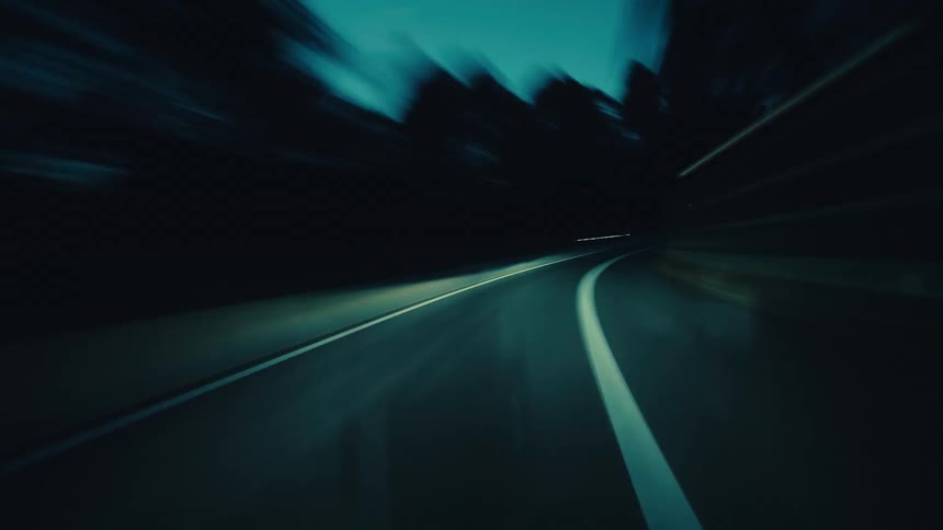 A stylized, fast-paced hyper-lapse from a driver's point of view speeds down a dark highway at dusk
