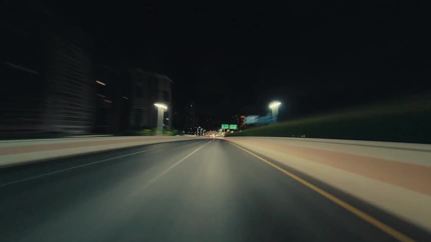 A high-speed hyperlapse from the perspective of a vehicle driving through a modern city at night and into a brightly lit tunnel