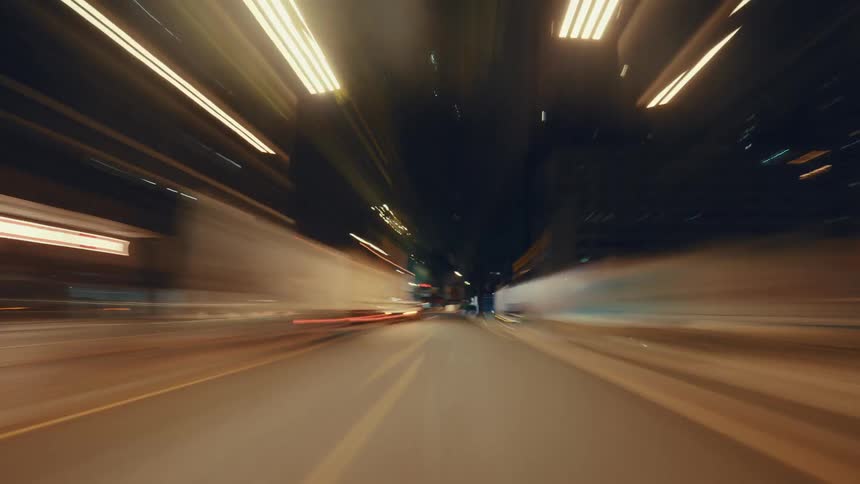 A fast-moving point-of-view hyper-lapse captures the vibrant light trails of a city street at night