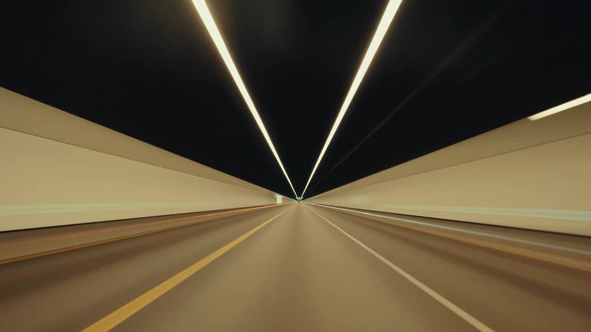 Futuristic POV timelapse of driving through a modern, illuminated highway tunnel at night, with light trails streaking past