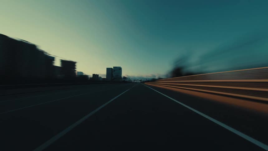 A cinematic low-angle hyper-lapse shows a fast-paced drive on a modern city highway as the sun sets
